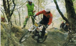 Observado por Nigel Birkett (Ossa); Mick sobre la Yamaha de fábrica, camino de ganar los 'Seis Días de Escocia de Trial' de 1974.